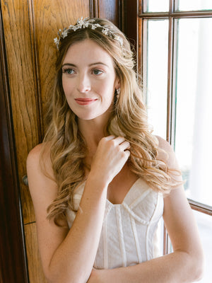 bride lining against a window wearing silver leaf and flower tiara with pearls and crystal stud earrings 