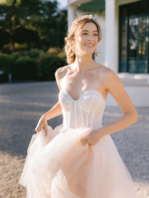 
            
                Load image into Gallery viewer, Bride running with a happy smile, wearing a flow wedding dress with matching bridal gold and blush accessories
            
        