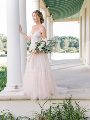 bride wearing a romantic gold blush floral with matching statement bridal earrings in a tulle blush gown holding a big arm vintage-inspired wedding bouquet made of roses and eucalyptus