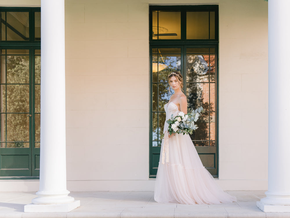 bride wearing a romantic gold blush floral with matching statement bridal earrings in a tulle blush gown holding a big arm vintage-inspired wedding bouquet made of roses and eucalyptus