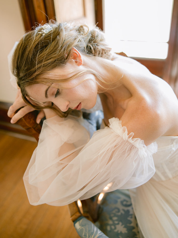 Bride resting on a vintage armchair wearing a sleeved pulled wedding gown and hair comb with blue crystals as her something blue