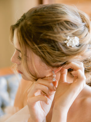 bride getting ready and putting on bridal jewellery such as silver crystal long drop earrings and a silver har comb